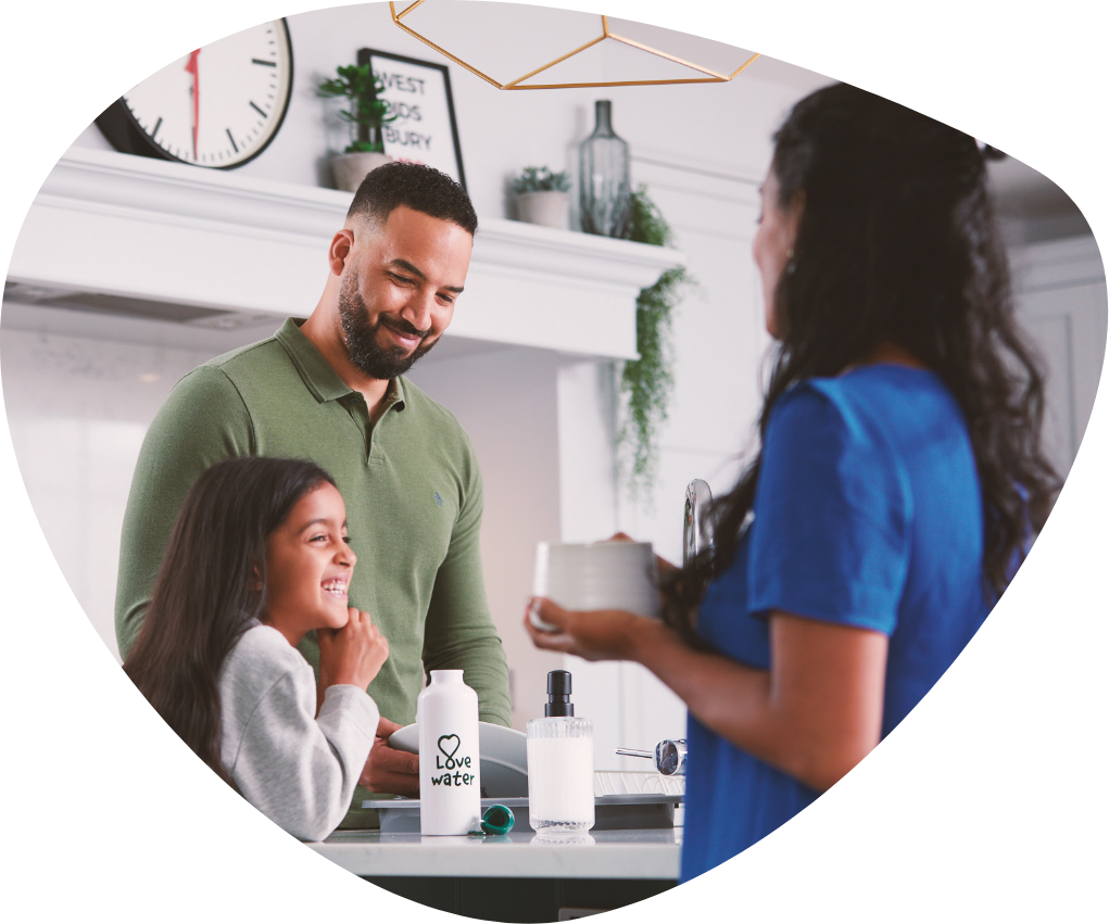 a smiling couple with there daughter with a bottle of water on the counter in front of them. The whole image is in the shape of a pebble.